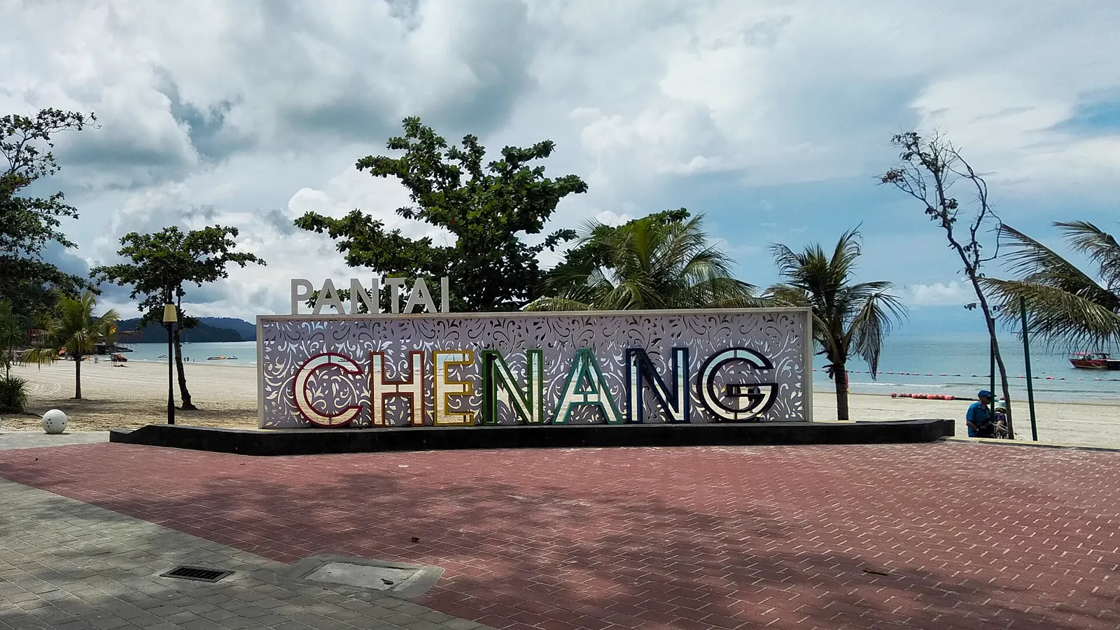 Pantai Cenang beach and its colourful landmark sign beneath tropical trees